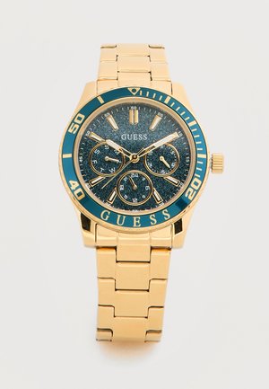 Montre-bracelet en métal doré avec cadran pailleté bleu, trois sous-cadrans, marqueurs dorés et logo "GUESS" sur la lunette et le cadran.