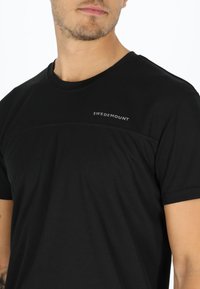 Mustapaitainen lyhythihainen t-paita, joka on valmistettu tekstuurikankaasta. Paitassa on vaakasauma ja vasemmassa yläkulmassa harmaa 'SWEDEMOUNT' logo.