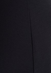 Gros plan sur un tissu noir lisse avec une couture verticale au centre, mettant en évidence la texture et les détails de la couture.