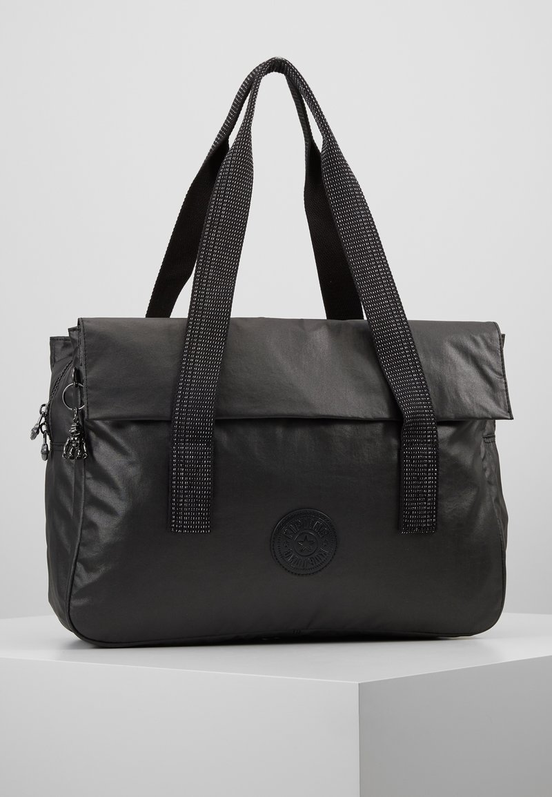 Sac cabas noir en matière souple avec deux sangles texturées, une fermeture à rabat et un logo rond sur le devant. Comprend une poche latérale zippée.