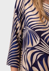 Satin garment with blue and beige palm leaf pattern. Features a loose fit and wide sleeves, highlighting the fluid texture and color contrast.