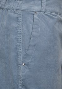 Světle modré kalhoty vyrobené z texturované látky, se boční kapsou a stříbrnými akcenty. Neformální design s elastickým pasem.