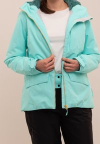 Une veste turquoise clair avec un zip à l'avant, une capuche doublée en polaire, deux poches avant et des détails de zip orange contrastants.