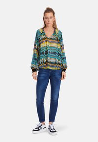 Multicolored polyester blouse with a V-neck, gathered neckline, and balloon sleeves, featuring a geometric pattern in blue, green, and yellow.