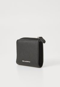 Μαύρο δερμάτινο πορτοφόλι με υφή, που διαθέτει κλείσιμο με φερμουάρ και ανάγλυφο λογότυπο στο μπροστινό μέρος. Συμπαγής και τετράγωνη σχεδίαση.