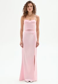 Vestido de dos piezas de color rosa que incluye un top corto ajustado con un detalle de encaje y una falda larga y recta con una abertura lateral, confeccionado en una tela suave.