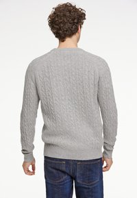 Szary sweter w warkoczowy splot z okrągłym dekoltem i ściągaczem, wykonany z miękkiego materiału. Nosi się go na ciemnych dżinsach, które prezentują teksturowane szwy.