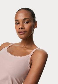 Camisole rosa chiaro con delicata rifinitura in pizzo lungo il colletto e le spalline, tessuto morbido con una superficie liscia, silhouette aderente.