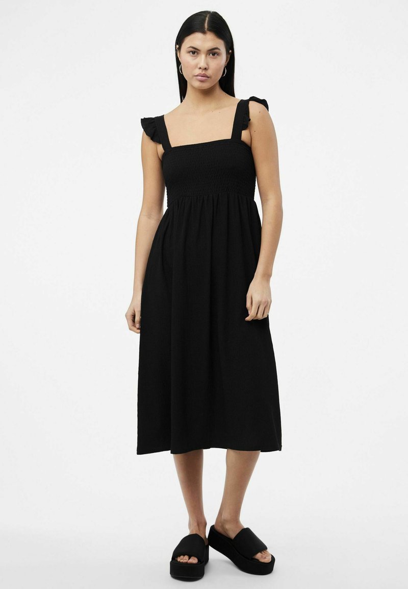 Μαύρο midi φόρεμα με τετράγωνη λαιμόκοψη, σφικτό μπούστο και λοξές τιράντες. Συνδυασμένο με μαύρες πλατφόρμες.