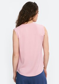 Różowa bluzka bez rękawów o gładkiej teksturze, okrągłym dekolcie i subtelnie zaokrąglonym dole. Tył ma czysty, prosty design bez zdobień.
