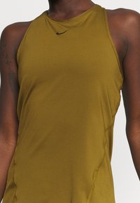 Detailní záběr na osobu v olivově zeleném bezrukávovém sportovním topu Nike s malým černým logem swoosh na hrudi.