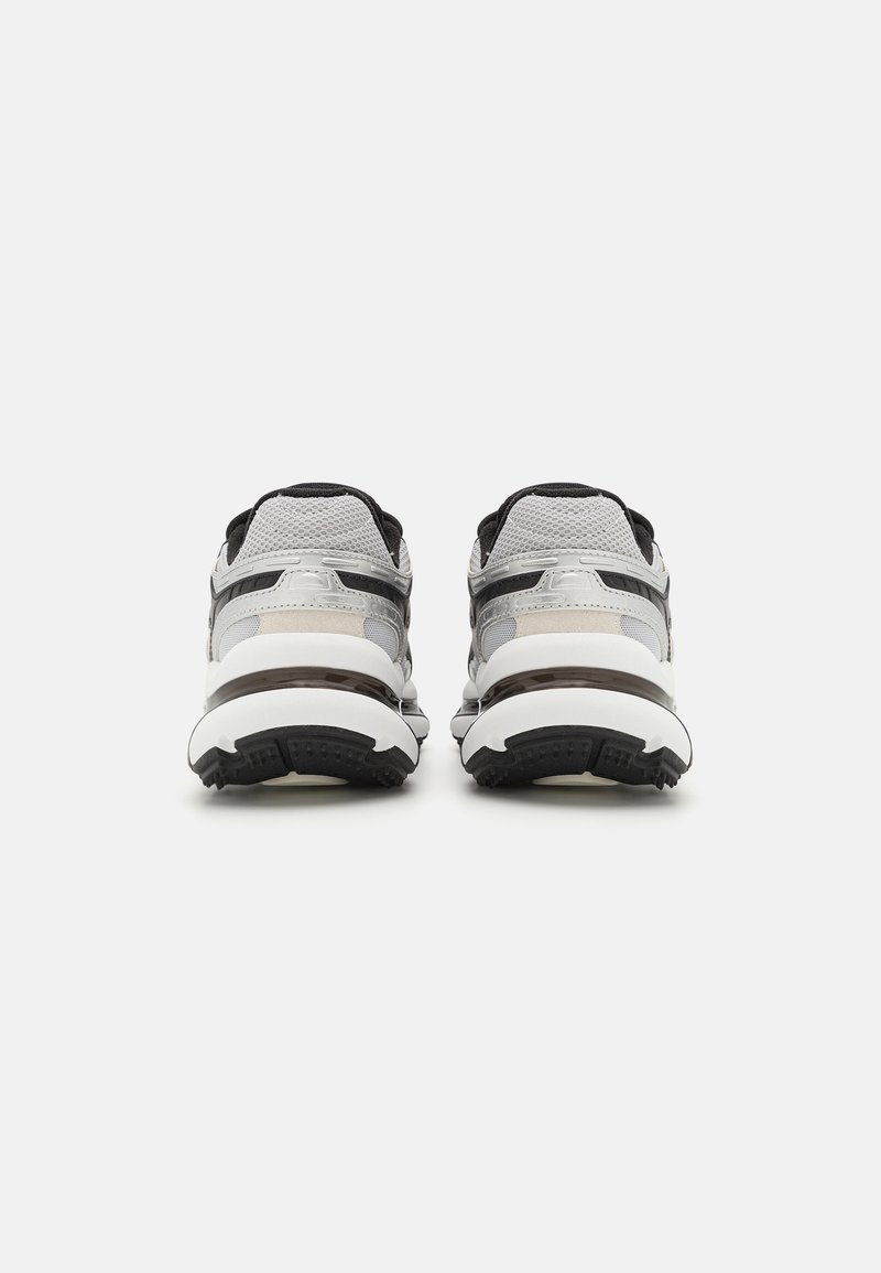 Buty sportowe z szarą siateczką na górze, czarnymi akcentami i grubą białą podeszwą środkową. Posiadają teksturowaną podeszwę zewnętrzną dla lepszej przyczepności.