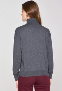 Maglione a collo alto grigio carbone con maniche lunghe, colletto e orlo a coste, texture morbida, vestibilità rilassata, abbinato a pantaloni bordeaux.