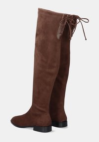 Botas de ante marrón hasta la rodilla con tacones bajos negros y detalles de cordones en la parte trasera.