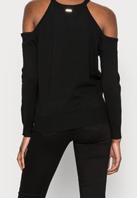 Pull noir épaules dénudées avec manches longues, ourlet côtelé et texture lisse, vue de dos, épaules découvertes.