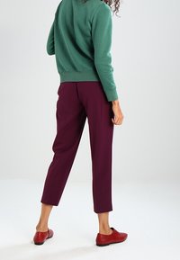 Zelená mikina s texturovanou tkaninou, doplněná o fialové kalhoty se slim fit. Celkový vzhled dotvářejí červené slip-on boty.