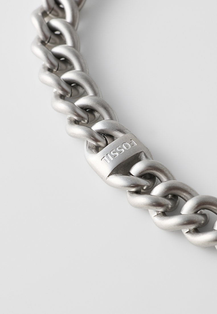 Pulsera de cadena de metal con eslabones entrelazados en tono plateado pulido, con un destacado grabado de la marca en uno de los eslabones.