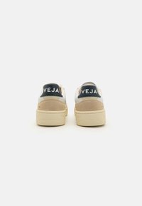 Beige Sneaker mit einem oberen Teil aus weißem Leder und hellbeigem Wildleder-Akzenten. Merkmale sind eine dunkelblaue Fersenkappe mit "VEJA"-Logo und einer strukturierten Gummisohle.