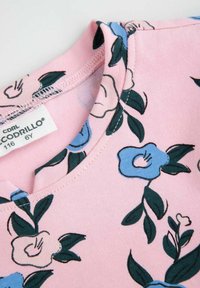 Różowa koszula baWEłniana z niebieskim i kremowym wzorem kwiatowym, okrągły dekolt i widoczne detale przeszycia. Metka głosi "Cocodrillo, rozmiar 116, 6 lat."