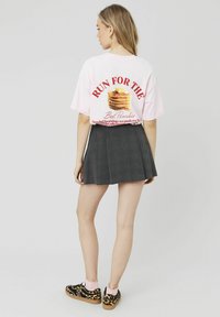 T-shirt rose clair oversize avec un graphique de pancake et du texte rouge, associé à une jupe à carreaux foncés et des chaussures noires à imprimé léopard.