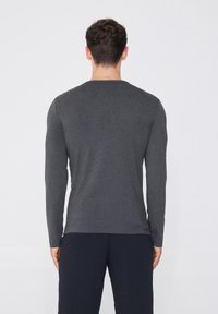 Graues langärmliges Shirt aus einem weichen, strukturierten Stoff mit Rundhalsausschnitt, von hinten betrachtet, kombiniert mit dunklen Hosen.