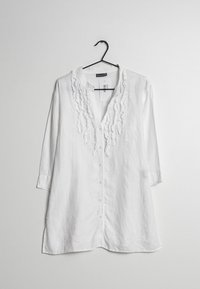 Camicia di lino bianca con maniche a tre quarti, caratterizzata da dettagli arricciati lungo il neckline e chiusura con bottoni sulla parte anteriore.