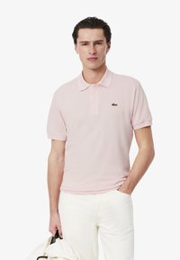 Ljusrosa polo skjorta i bomull, med klassisk krage, korta ärmar och en grön broderad logotyp på vänster bröst.