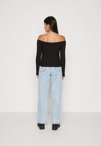 Haut noir à épaule dénudée avec des manches longues, associé à un jean large bleu clair et des chaussures noires chunky, vu de dos.