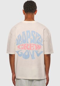 Cremefarvet oversized t-shirt med en iøjnefaldende, multikolor grafisk tekst, der står 'DROPSIZE CREW LOVE' i blå og lyserøde nuancer på ryggen.