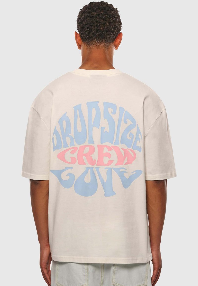 Cremefarvet oversized t-shirt med en iøjnefaldende, multikolor grafisk tekst, der står 'DROPSIZE CREW LOVE' i blå og lyserøde nuancer på ryggen.