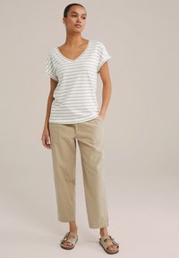 Triibuline lühikeste varrukatega V-kaelusega T-särk koore ja beeži värviga, koos heleda beeži vabalt jalgu jääva pükste ja roheliste sussidega.