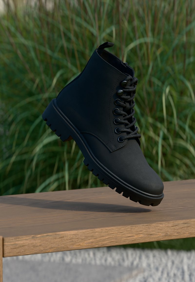 Botte noire à lacets flottant au-dessus d'un banc en bois avec de l'herbe verte floue en arrière-plan.