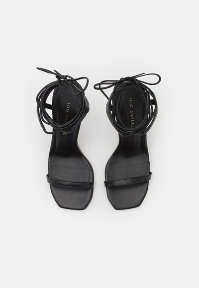 Sandalias de tacón negro con puntera cuadrada, con finas tiras cruzadas y largas cintas para atar. Textura de cuero suave, diseño minimalista.
