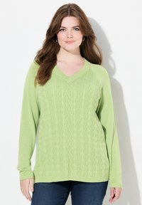 Vaaleanvihreä neulottu villapaita, jossa on V-pääntie, jalokivikaulustyylinen kuviointi ja pitkät hihat. Yhdistetty tummansinisiin farkkuihin.