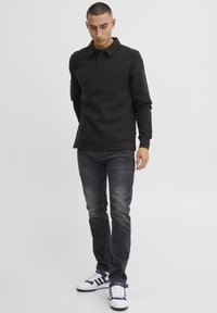 Svart langermet polo med krage og knappestolpe, kombinert med mørke jeans og hvite sneakers med marineblå detaljer.
