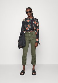 Blusa preta de manga longa com padrão floral, calças cropped de cintura alta em verde militar com detalhes bordados na bainha, e sandálias pretas sem fecho.