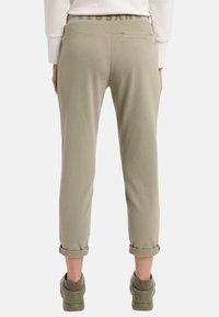 Helle olivgrüne Sweatpants mit einem gerippten Bund, hochgekrempelten Säumen und einer Gesäßtasche. Glattes Material mit einer lässigen, entspannten Passform.