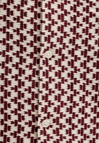 Gros plan sur un tissu tricoté à motifs crème et bordeaux avec deux boutons blancs le long d'une couture centrale.