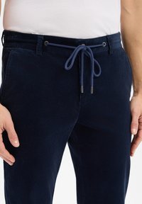 Navy corduroy trousers with an elastic waistband, a drawstring closure, and subtle ribbed texture. Features side pockets for storage.