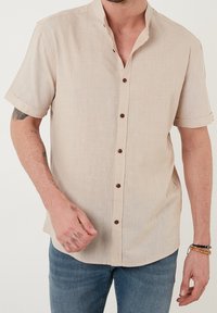 Lichtbeige kortste mouw button-up shirt gemaakt van een textuurstof, met een smalle kraag en bruine knopen aan de voorkant.