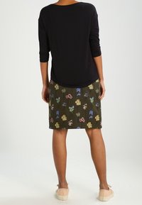 Top negro de manga larga combinado con una falda verde de estampado floral que presenta un bordado colorido y un ajuste ceñido, vista desde atrás.