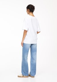 Weißes Baumwoll-T-Shirt mit kurzen Ärmeln, lockerer Passform und Rundhalsausschnitt, kombiniert mit hellblauen weit geschnittenen Jeans und beigen Sneakers.