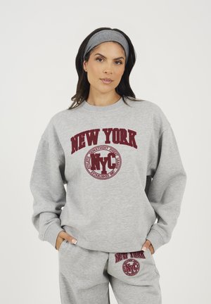 Grijze sweatshirt en joggingbroek set met een bordeauxrode "NEW YORK" grafiek en embleem. Zachte stof, losse pasvorm, met ribbenboorden aan de mouwen en tailleband.