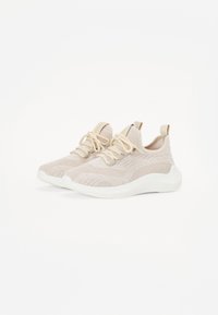 Baskets de sport beige clair avec une tige en maille texturée, des lacets élastiques et une épaisse semelle blanche. Présente un tirant à l'arrière.