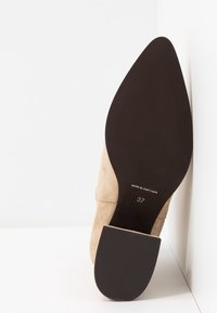 Chaussure à talons aiguilles en suède beige avec un bout pointu et une semelle en caoutchouc noir texturé. Taille 37 marquée sur le côté intérieur.