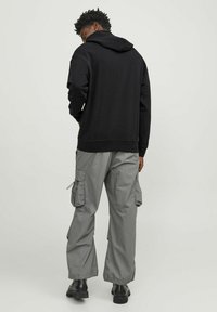 Black hooded sweatshirt, cotton material, relaxed fit, paired with gray cargo pants featuring multiple side pockets, and black boots.