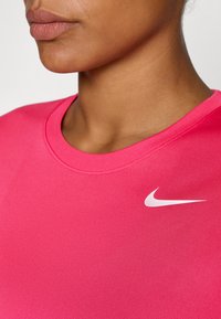 Rózsaszín Nike sportpóló, kerek nyakkivágással, bal oldalon fehér swoosh logóval. Simább textúra és testhez álló fazon.
