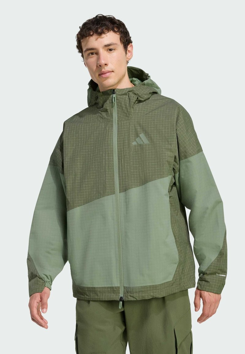 Vihreä tuulitakki, jossa huppu, erilaiset pintakuvioinnit, yläosassa ruutukuvio ja vetoketjulliset taskut.