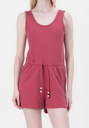 Femme portant une combinaison sans manches rose foncé avec une taille coulissante et un short sur fond blanc uni.