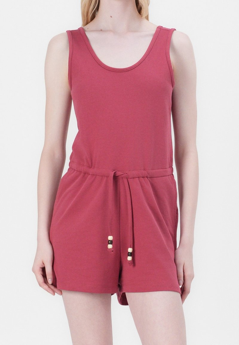 Femme portant une combinaison sans manches rose foncé avec une taille coulissante et un short sur fond blanc uni.